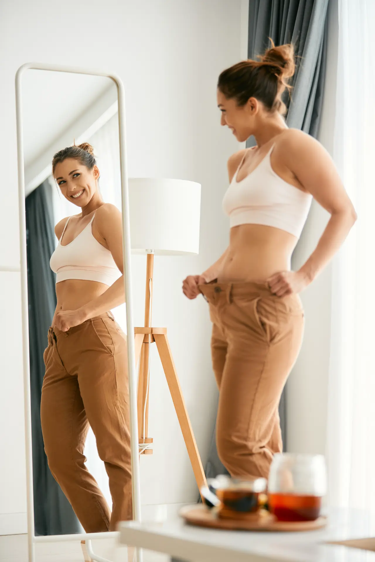 Woman checking her looser waistband in a mirror at home