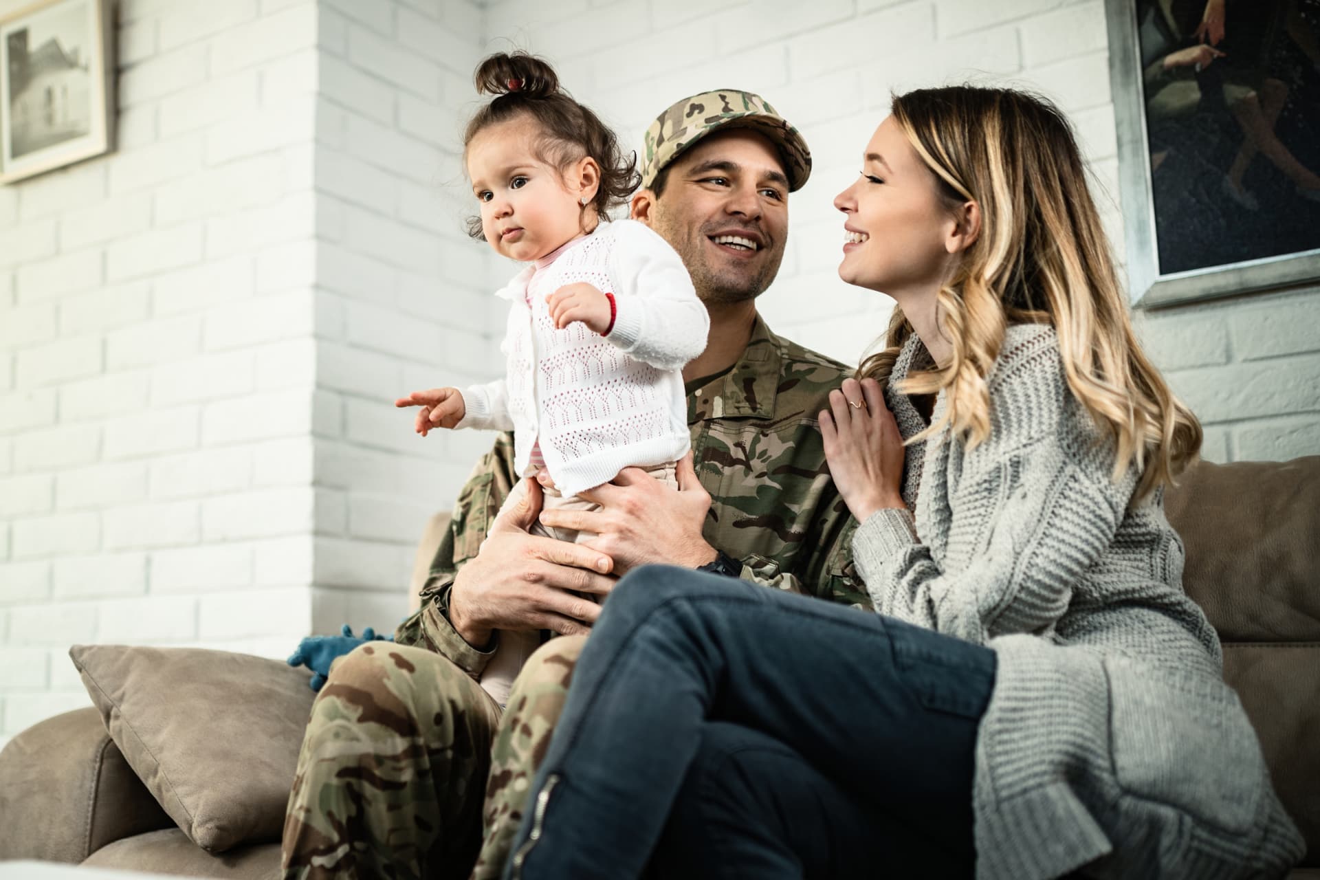 Service member in uniform at home with his wife and young daughter