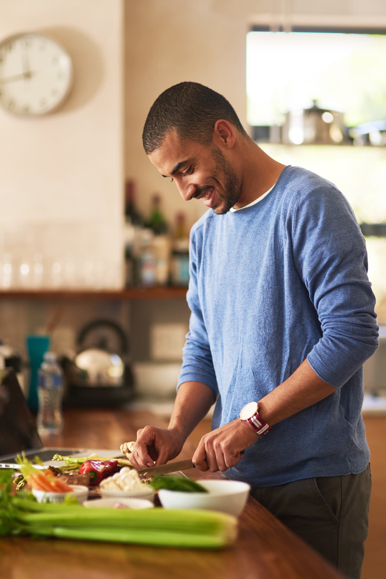 Man smiling while chopping fresh vegetables in a sunlit kitchen