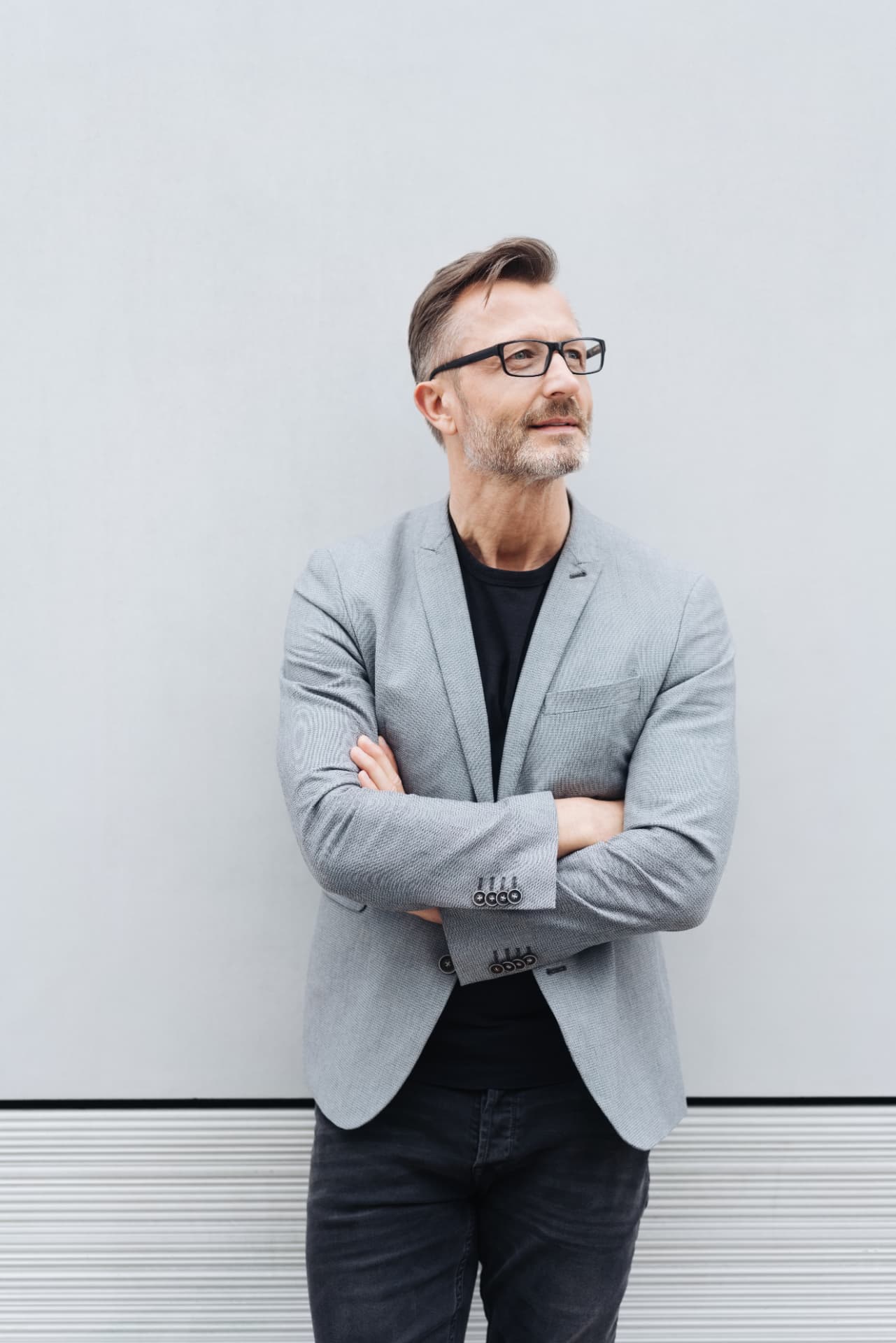 Man in a grey blazer standing against a light wall