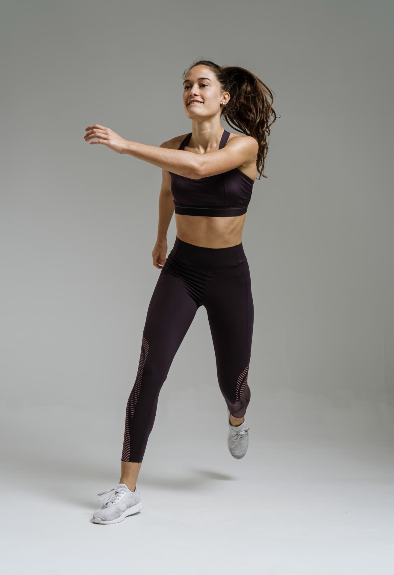 Woman in athletic wear mid-stride against a soft studio backdrop
