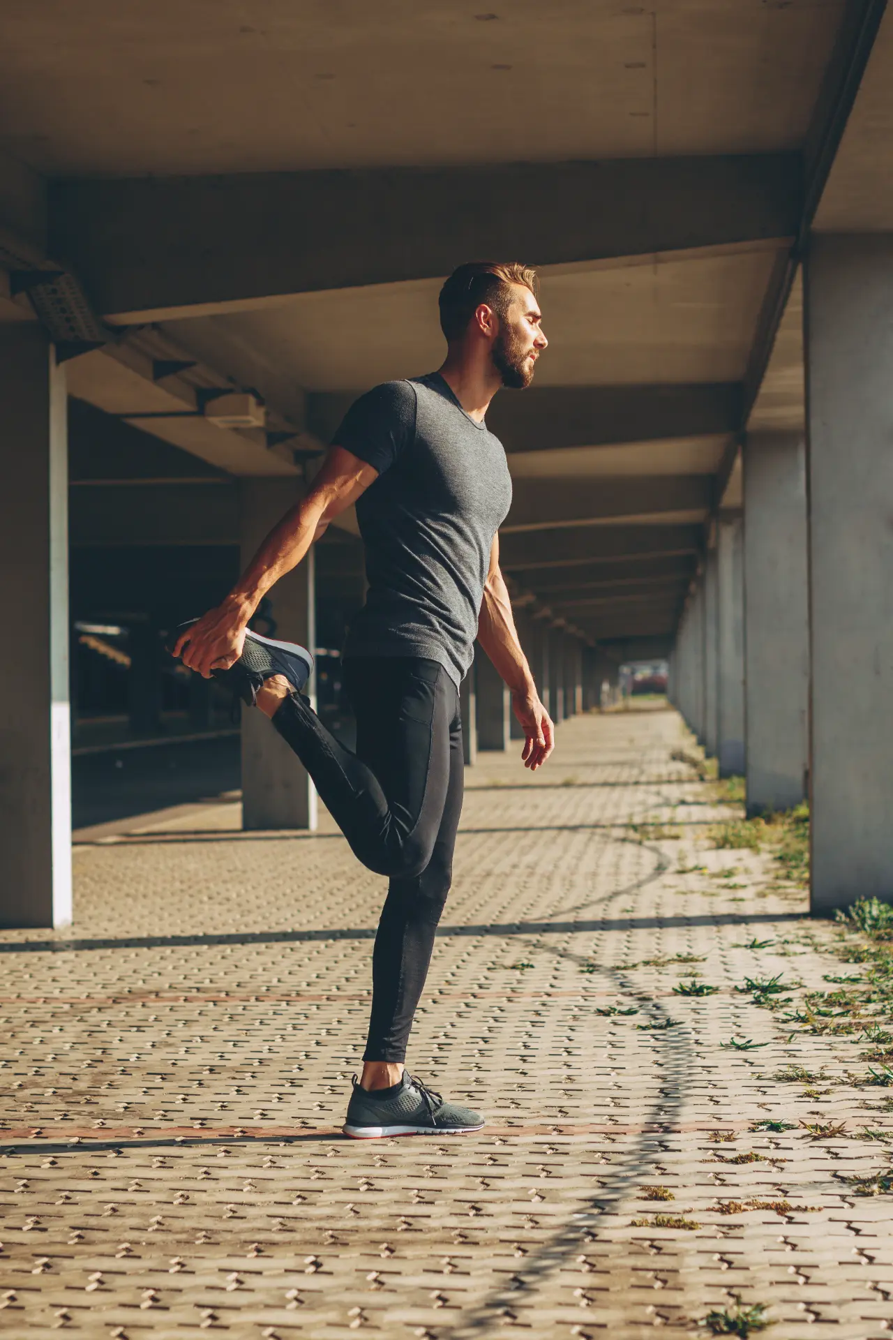 Man stretching in warm sunlight under a concrete colonnade
