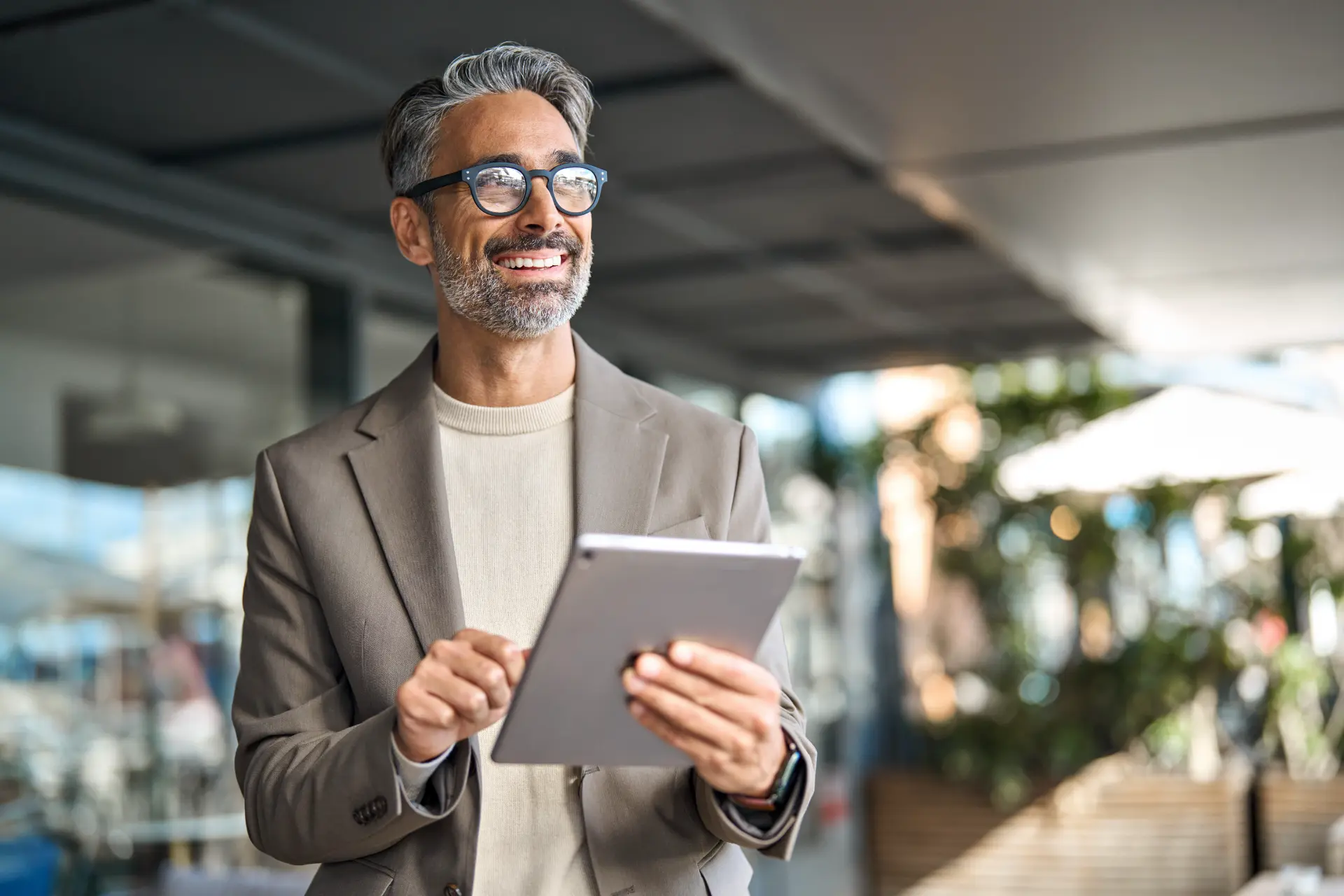 Confident man smiling outdoors while holding a tablet